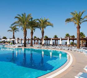 Großer Pool mit klarem Wasser, umgeben von Liegestühlen und Palmen unter blauem Himmel.