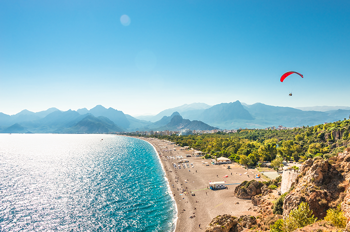 Ein Paraglider fliegt über eine malerische Küste und beeindruckende Berge, ein Bild von Freiheit und Naturverbundenheit.