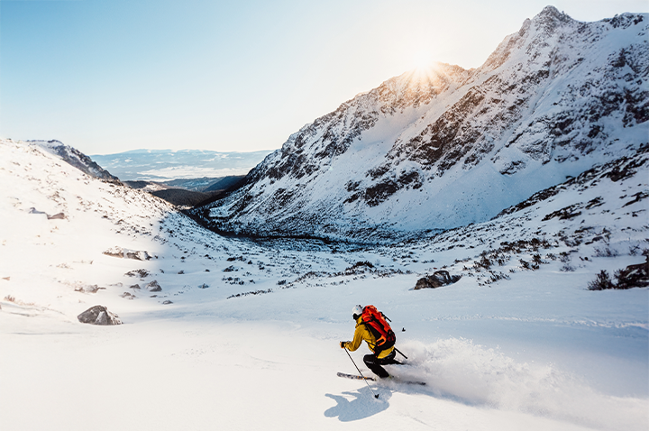Eine Person genießt das Skifahren auf einem schneebedeckten Berg, während die Sonne über der Winterlandschaft scheint.