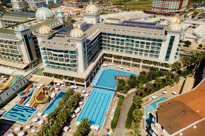 Luftaufnahme eines großen Hotelkomplexes mit mehreren Pools, Wasserrutschen und Palmen vor dem Gebäude.