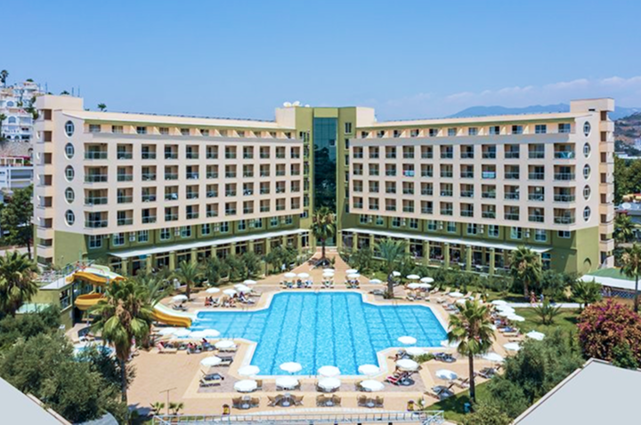 Großes Hotelgebäude mit mehreren Stockwerken, zentralem Eingangsbereich, zwei Wasserrutschen und einem großen Pool mit Liegestühlen im Innenhof.