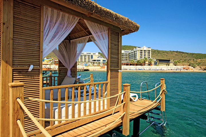 Charmantes Holzhaus auf dem Wasser mit einem schützenden Dach und das Hotel im Hintergrund, ideal für einen erholsamen Hotelaufenthalt