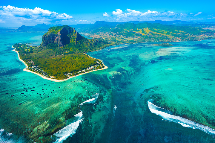 Luftaufnahme einer tropischen Insel in Mauritius, umgeben von klarem, blauem Ozean und üppigem Grün.
