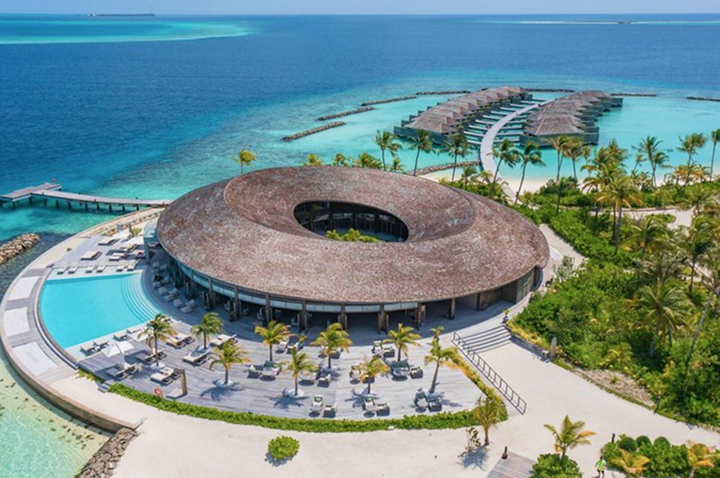 Rundes, strohgedecktes Gebäude mit Innenhof an einem Strand mit Palmen und über Wasser gebauten Bungalows. Rundes, strohgedecktes Gebäude mit Innenhof an einem Strand mit Palmen und über Wasser gebauten Bungalows.