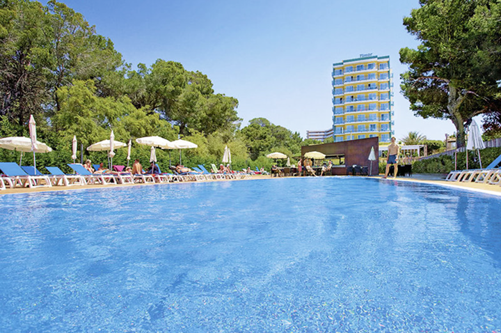 Großer rechteckiger Hotelpool mit Liegestühlen und Sonnenschirmen an den Seiten sowie einem mehrstöckigen Hotelgebäude im Hintergrund.