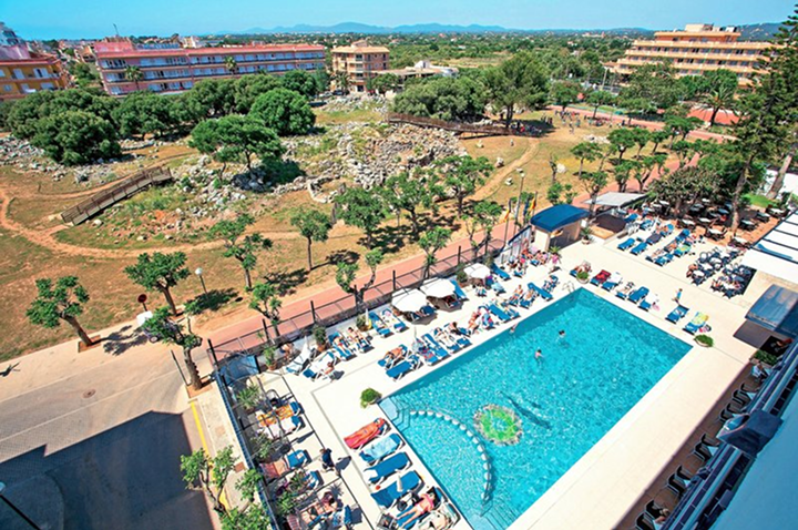 Hotelpool mit Liegestühlen und Sonnenschirmen neben einer archäologischen Ausgrabungsstätte und mehreren mehrstöckigen Gebäuden im Hintergrund. Hotelpool mit Liegestühlen und Sonnenschirmen neben einer archäologischen Ausgrabungsstätte und mehreren mehrstöckigen Gebäuden im Hintergrund.