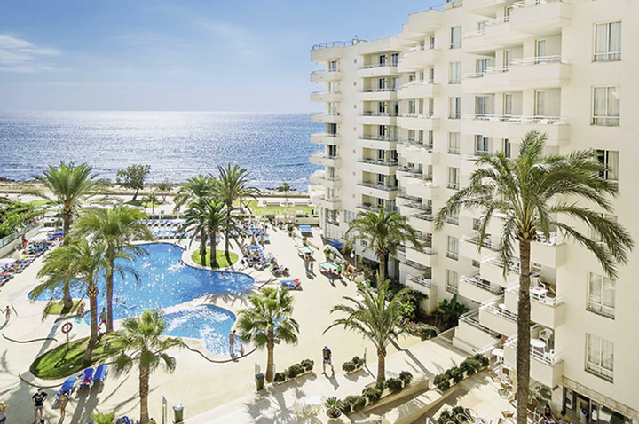 Blick auf den Pool und den Strandbereich des Hotels, umgeben von Palmen und Sonnenliegen.