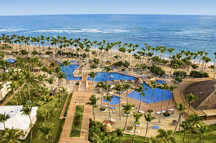 Blick auf eine weitläufige Hotelanlage mit mehreren Pools, Palmen und direktem Zugang zum Meer.