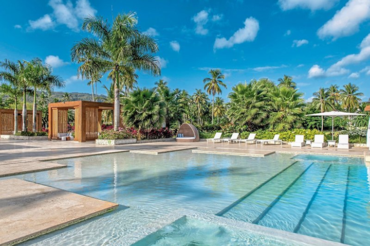 Moderner Außenpool mit Liegestühlen, Sonnenschirm und Palmen im Hintergrund.