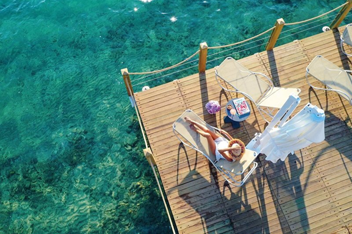 Eine Frau sitzt auf einem Holzsteg in einem Stuhl unter einem Sonnenschirm, umgeben von der Atmosphäre eines Hotels. Eine Frau sitzt auf einem Holzsteg in einem Stuhl unter einem Sonnenschirm, umgeben von der Atmosphäre eines Hotels.